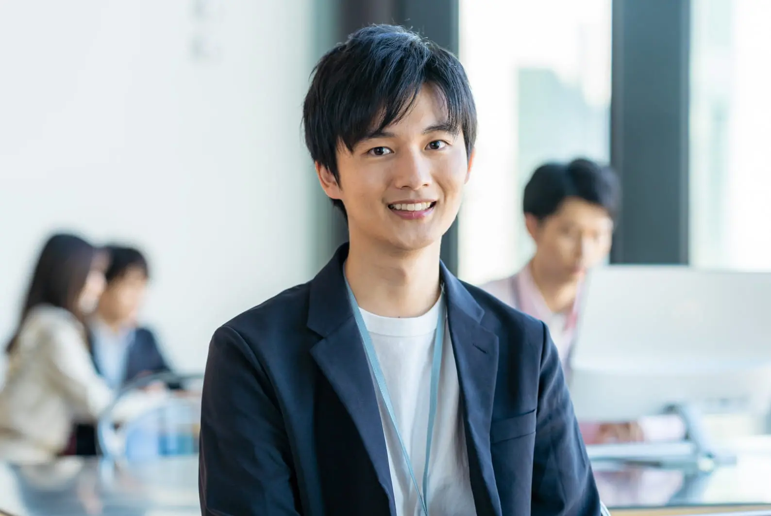 笑顔の男性の写真。背景では同僚たちが仕事をしている