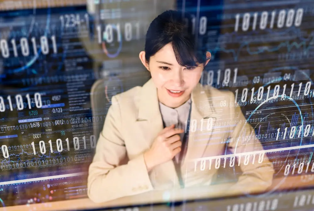 モニターに映るデータを背景に、作業をする女性エンジニア