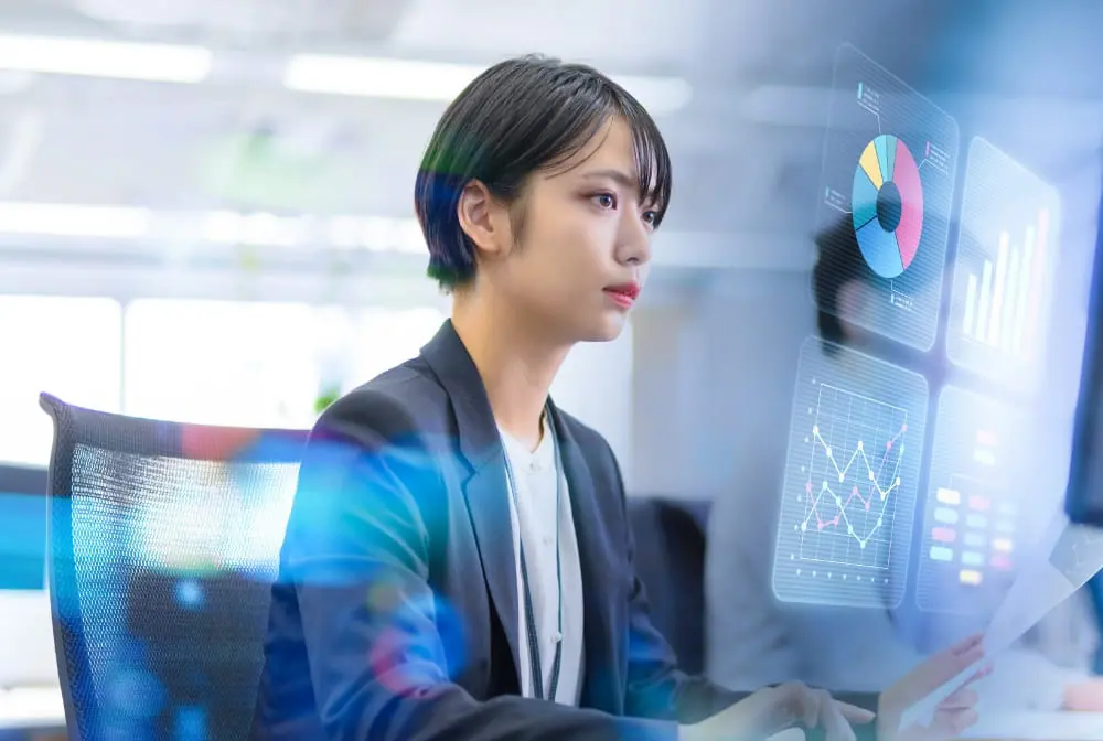 オフィスでデータ分析を行う女性エンジニア。グラフやチャートを表示したモニターを見ながら業務に集中している